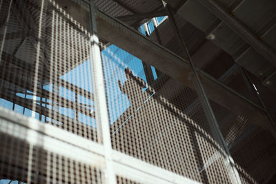 Low angle view of man standing by window seen through fence