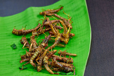 Pile fried grasshoppers ready to eat on green leaf banana