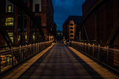 Footbridge in city against sky at night