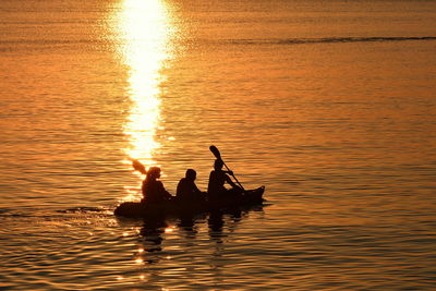 Silhouette of people paddling at sunset