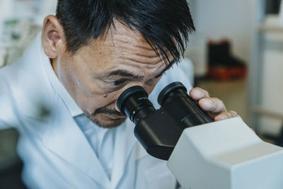 Male scientist looking though microscope while man standing in background at laboratory