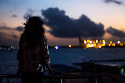 Rear view of woman standing on bridge on sea at dusk