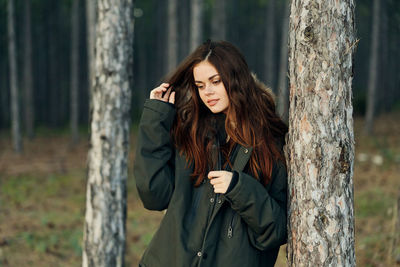 Young woman standing by tree trunk in forest