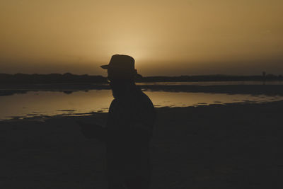 Silhouette man standing on beach against sky during sunset