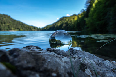 Close-up of crystal ball on rock by lake against sky