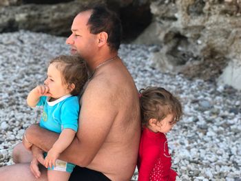 Shirtless man with children sitting at beach