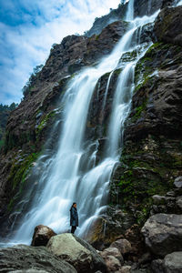 Waterfall white water stream falling from mountains with girl standing nearby at day