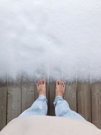 Low section of man standing on snow covered boardwalk