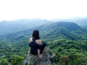 Rear view of woman sitting on rock against sky