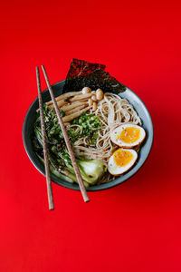 Top view of ceramic bowl with delicious ramen and chopsticks placed on red background