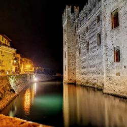 Illuminated buildings by river in city at night