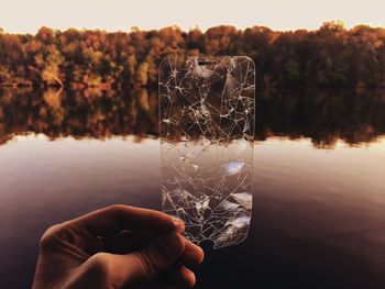 Cropped hand holding cracked glass against lake