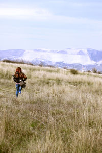 Rear view of woman walking on field against sky