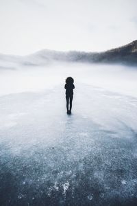 Rear view of woman standing on frozen lake against sky