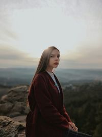 Young woman looking away while standing on rock against sky