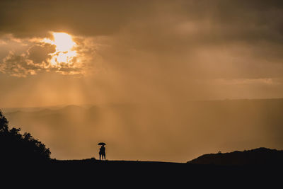 Silhouette person standing on mountain against sky during sunset