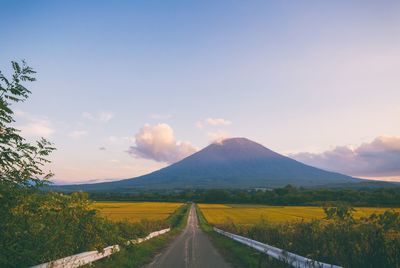 Country road along landscape and mountains against sky