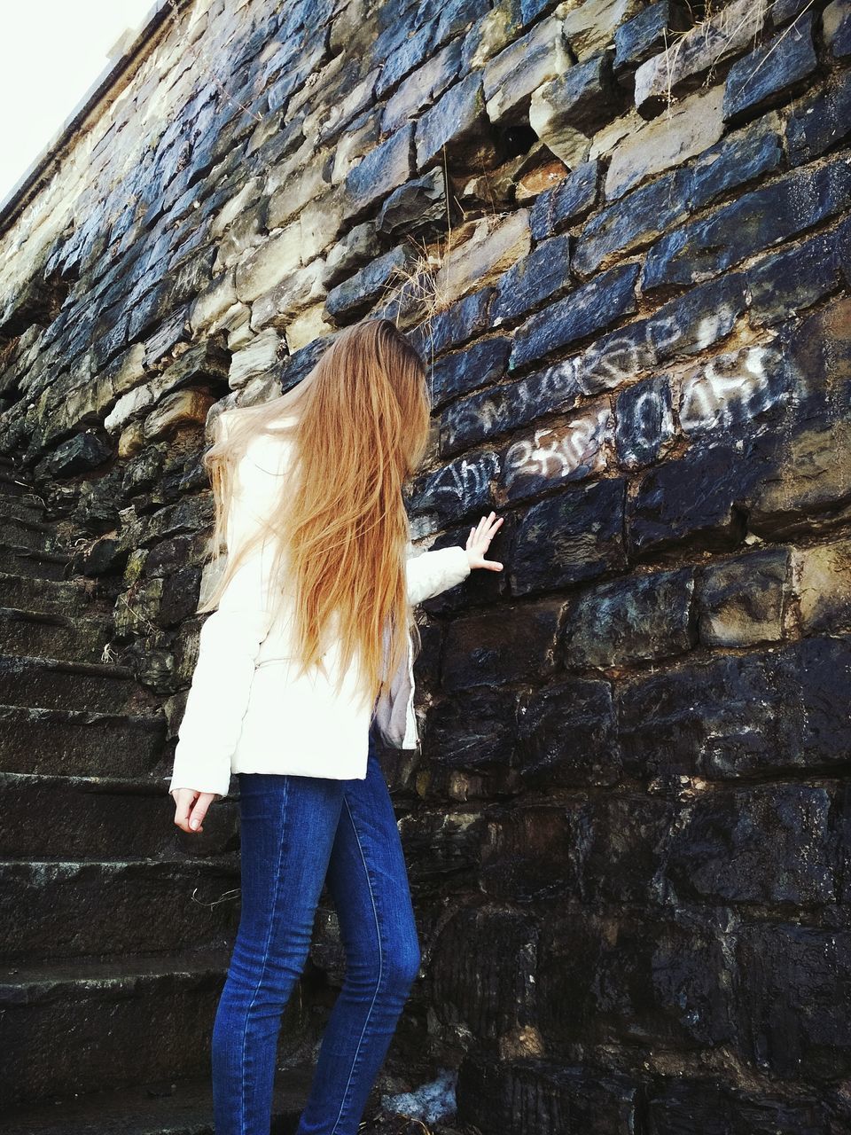 REAR VIEW OF WOMAN STANDING AGAINST THE WALL