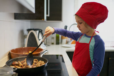 Girl in red chef's hat frying meat in a pan at home
