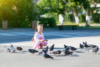 Portrait of girl feeding pigeons on footpath