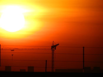 Silhouette crane against orange sky during sunset