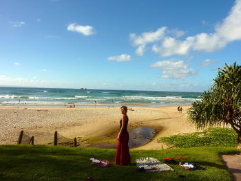 Full length of woman standing on grass at beach against sky