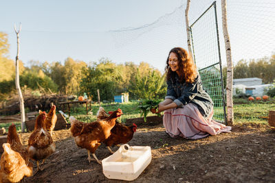 Happy middle aged woman on a private farm feeding chickens