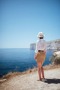 Rear view of woman standing at beach against sky
