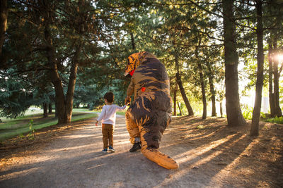 Rear view of boy walking with person wearing dinosaur costume in park