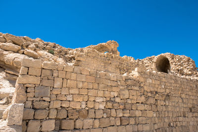 Low angle view of stone wall against clear blue sky