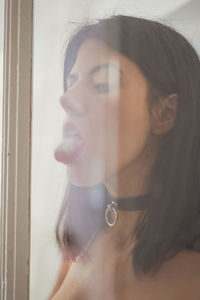 Close-up of woman licking glass window at home