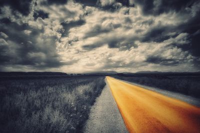 Tire tracks on road against cloudy sky