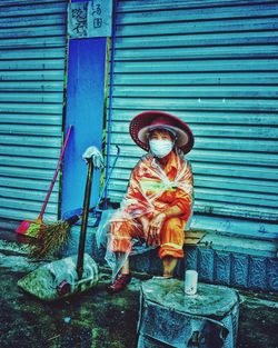 Portrait of woman in mask sitting against shutter