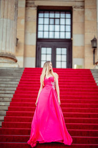 Female model wearing pink evening gown while standing on steps