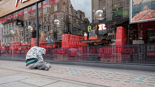 Man sitting on footpath by street in city