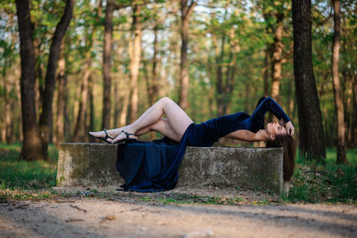 Full length of woman relaxing on tree trunk in forest