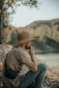 Side view of man wearing hat while sitting on land