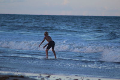 Full length of shirtless man in sea against sky