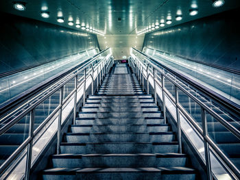 Low angle view of steps amidst escalator in illuminated subway station