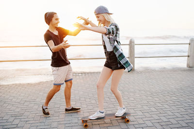 Full length of man teaching skating to girlfriend against sea