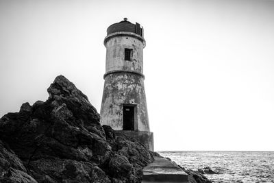 Lighthouse by sea against clear sky