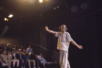 Low angle view of young male keynote speaker with braided hair gesturing while explaining in seminar at theater