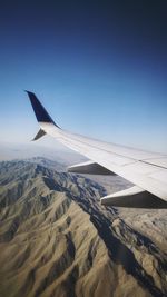 Airplane flying over mountains against clear blue sky