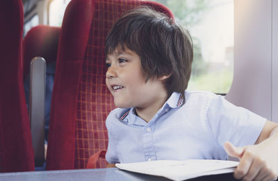 Smiling boy looking away while sitting with book in train