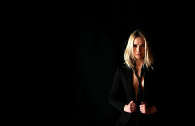Portrait of woman wearing suit while standing against black background