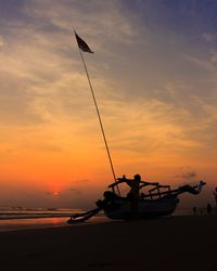 Silhouette boat moored at beach against sky during sunset