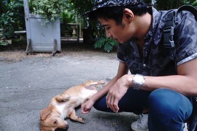 Young man petting puppy lying on road