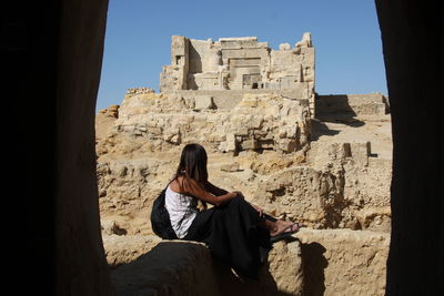 Woman sitting on stone against old ruins