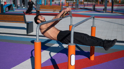 Shirtless man doing horizontal balance on parallel bars at sports ground. 