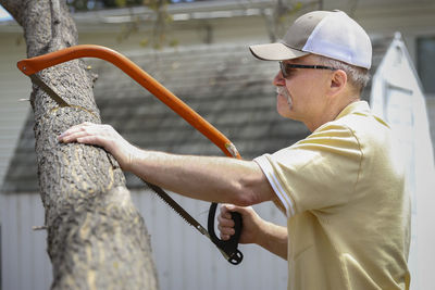 Side view of senior man sawing tree outdoors